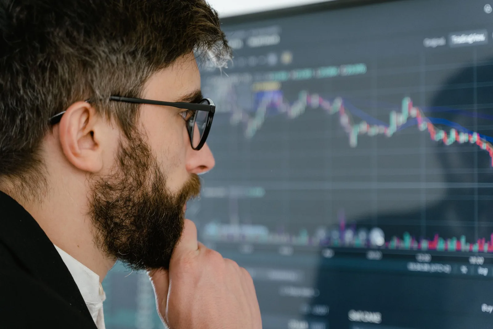 Economist staring at stock market charts on a screen looking confused and thoughtful